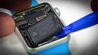 Wymiana baterii Apple Watch: wyjmowanie starego ogniwa za pomocą niebieskiego narzędzia.