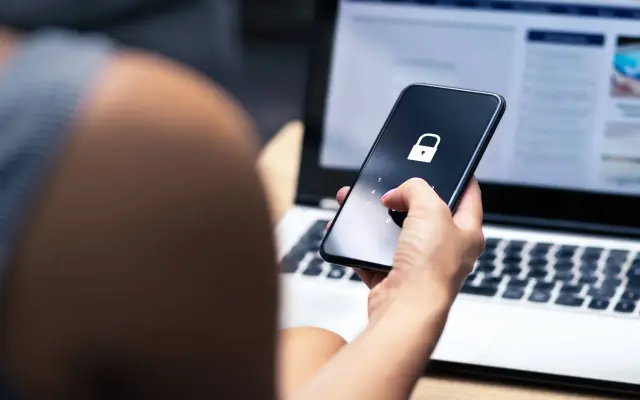 Dłoń z różowym lakierem do paznokci wpisuje kod PIN na ekranie telefonu z ikoną kłódki. Dowiedz się, jak usunąć wirusy z telefonu.