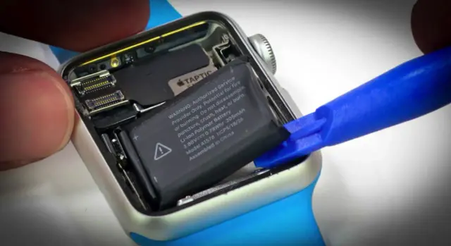 Wymiana baterii Apple Watch: wyjmowanie starego ogniwa za pomocą niebieskiego narzędzia.
